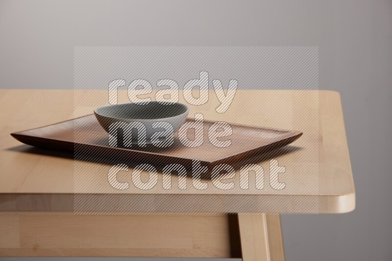 grey bowl placed on a rectangular wooden tray on the edge of wooden table