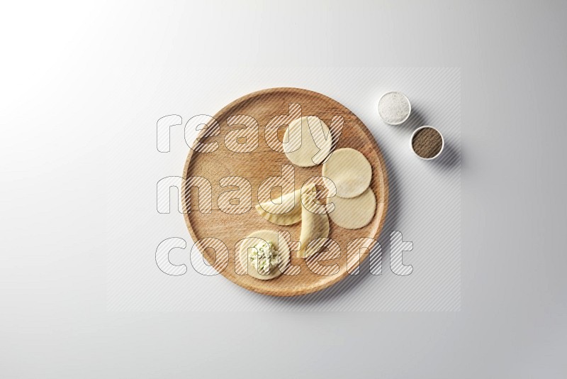 two closed sambosas and one open sambosa filled with cheese while salt, and black pepper aside in a wooden dish on a white background