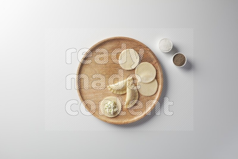 two closed sambosas and one open sambosa filled with cheese while salt, and black pepper aside in a wooden dish on a white background