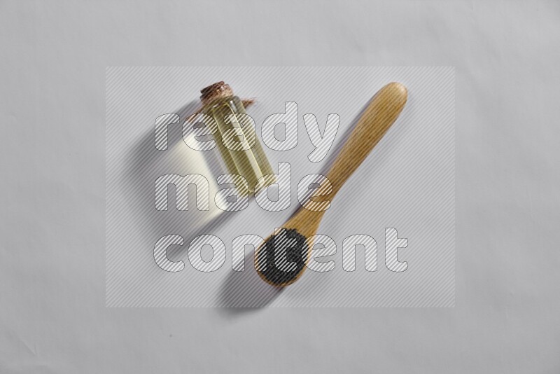 ملعقة خشبية ممتلئة ببذور حبة البركة مع زجاجة من زيت حبة البركة على أرضية بيضاء