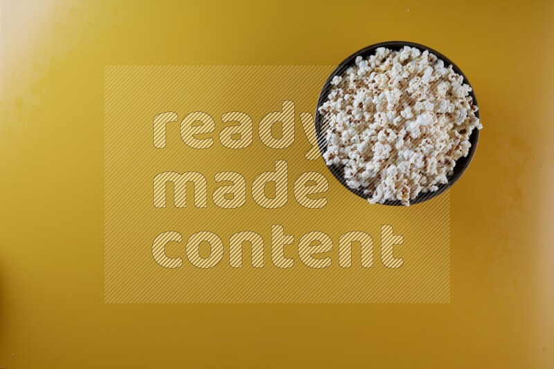 A copper ceramic bowl full of popcorn on a yellow background in different angles