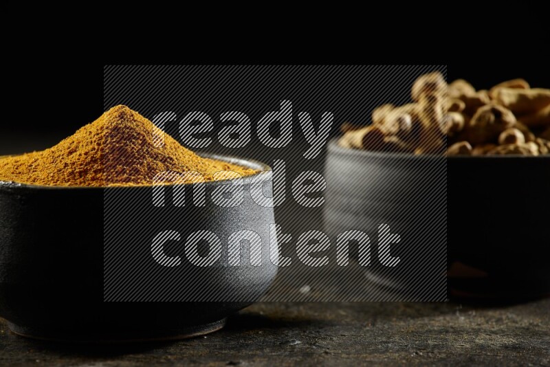 وعاءان من الفخار باللون الأسود، أحدهما ممتلئ ببودرة الكركم والآخر ممتلئ بأصابع كاملة من الكركم المجفف على خلفية سوداء