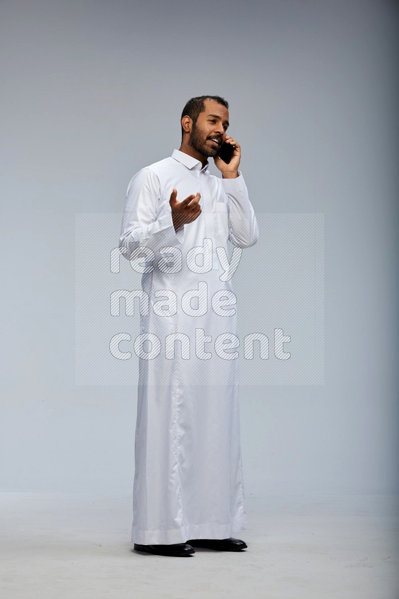 Saudi man wearing Thob standing talking on phone on Gray background