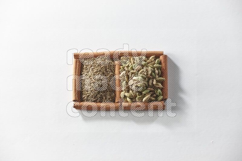 مربعان من أعواد القرفة ممتلئان بحبوب الهيل والكمون علي خلفية بيضاء