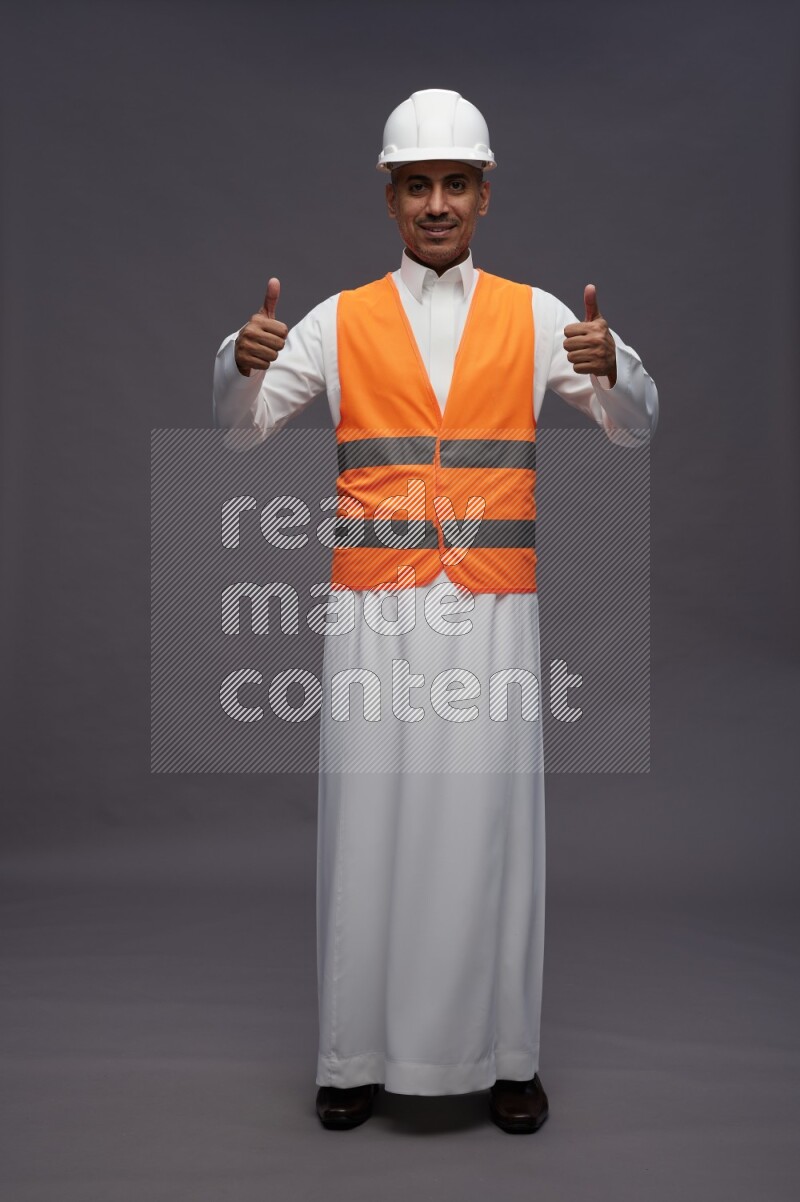Saudi man wearing thob with engineer vest standing interacting with the camera on gray background