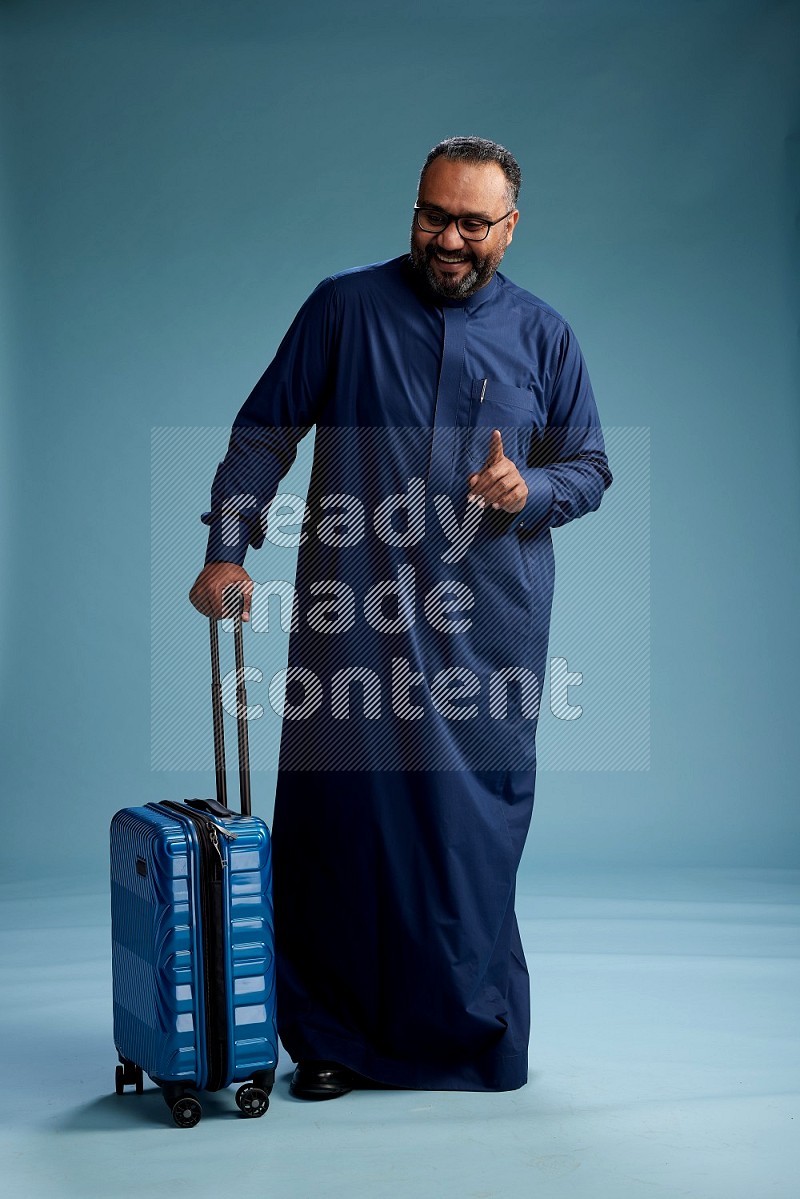 Saudi Man without shimag Standing pulling travel bag on blue background