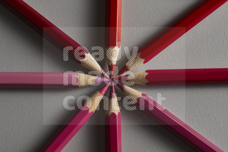 An arrangement of colored pencils in shades of pink and red on grey background