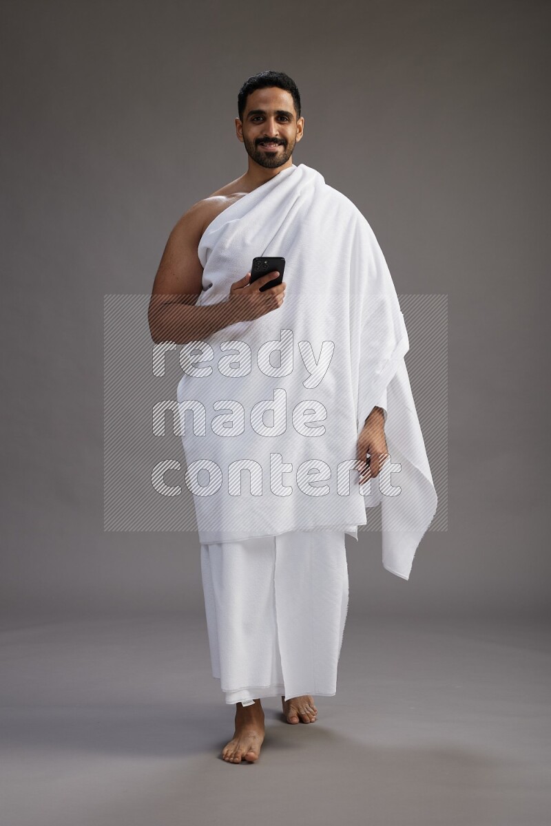 A man wearing Ehram Standing texting on phone on gray background