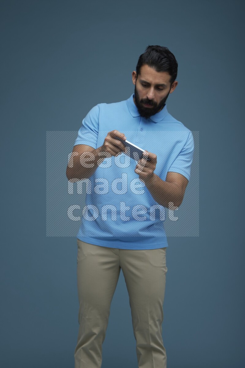 Man playing a game on his phone in a blue background wearing a Blue shirt