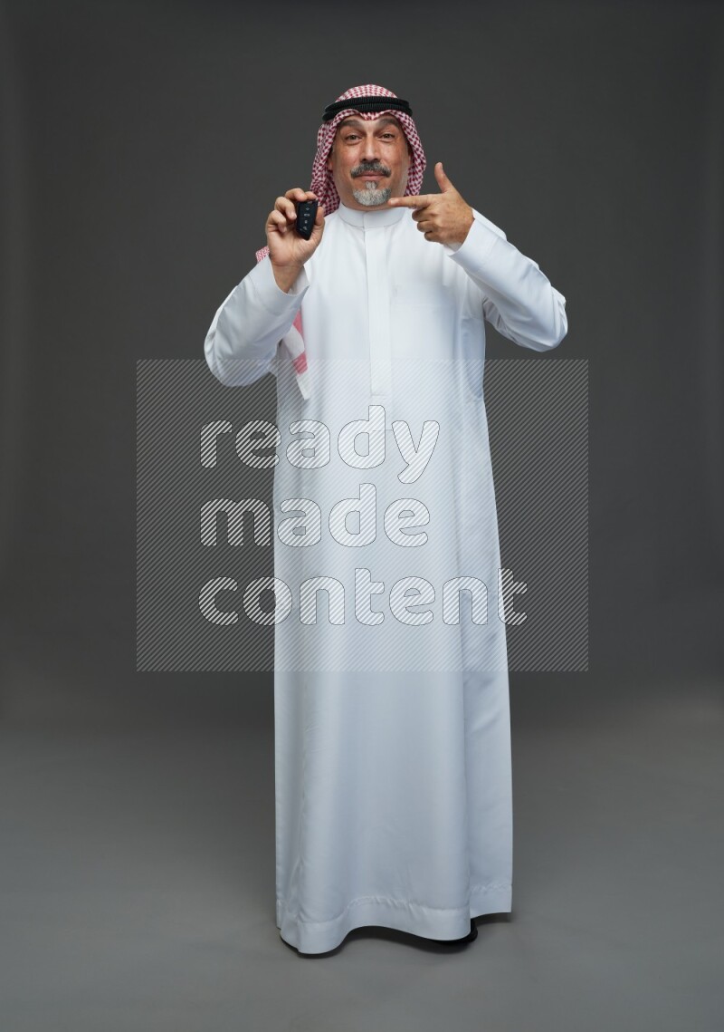 Saudi man with shomag Standing holding car key on gray background