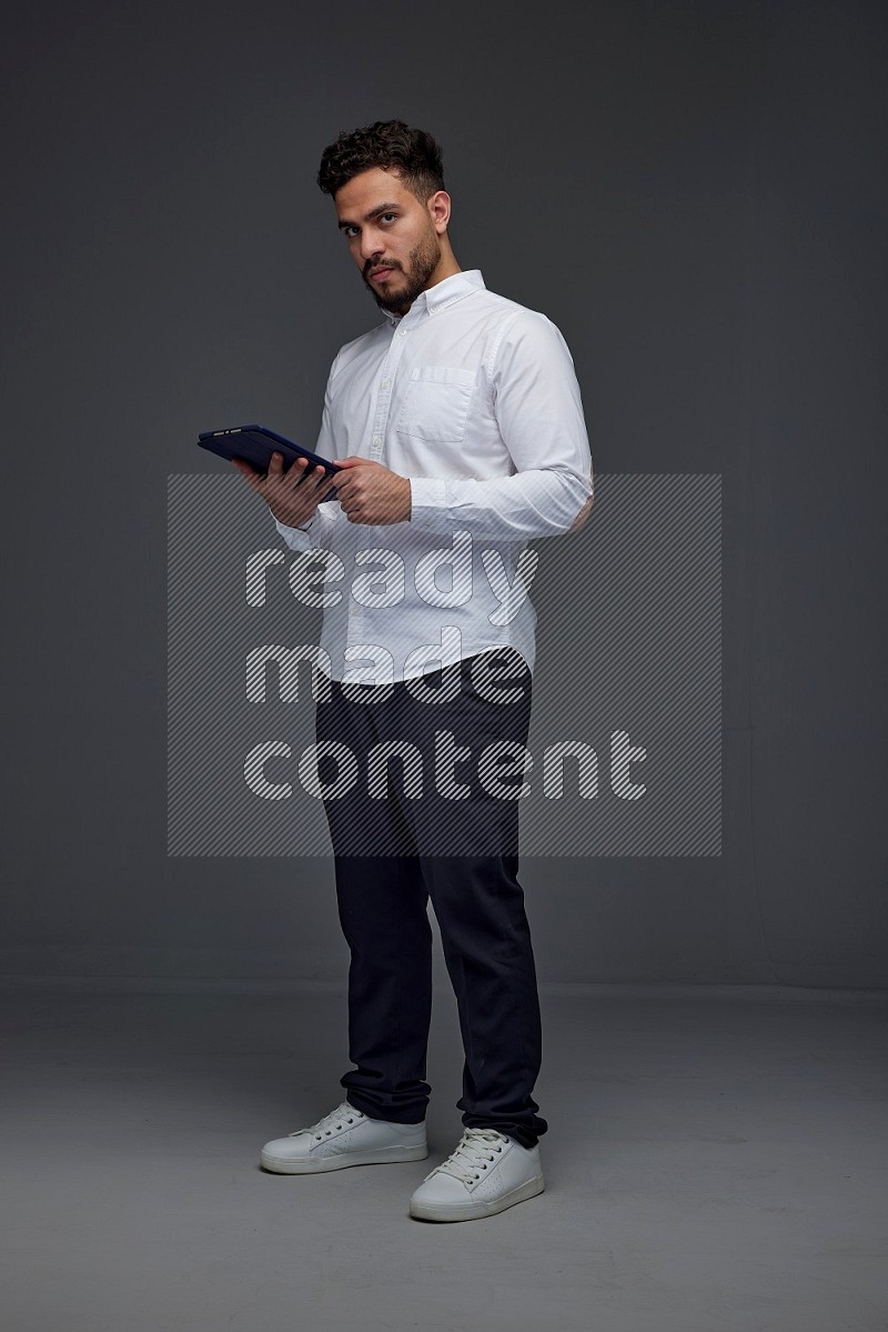 A man wearing smart casual standing and using his tablet eye level on a gray background