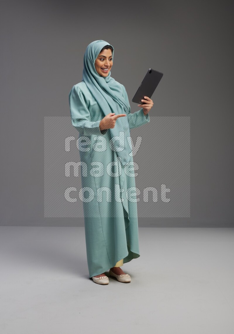 Saudi Woman wearing Abaya standing working on tablet on Gray background