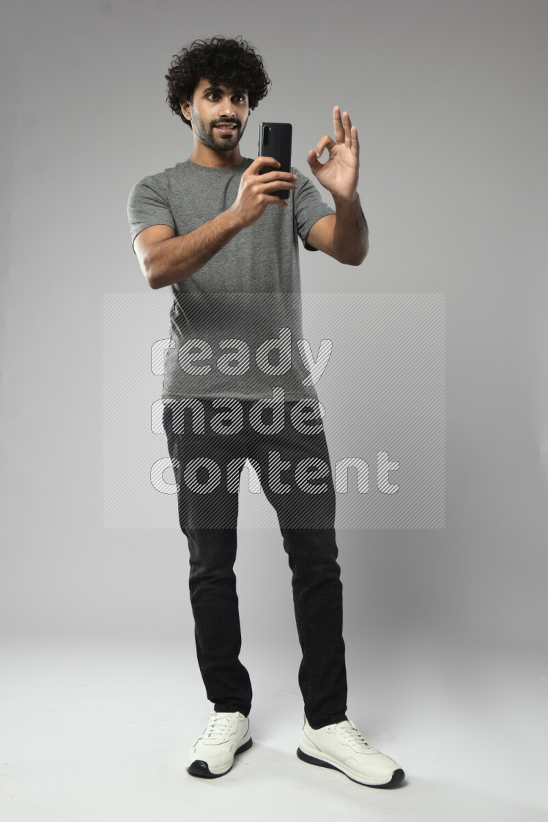 A man wearing casual standing and shooting with his phone on white background