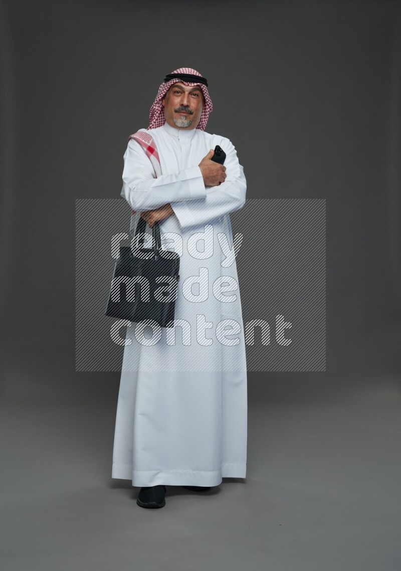 Saudi man with shomag Standing holding bag and phone on gray background