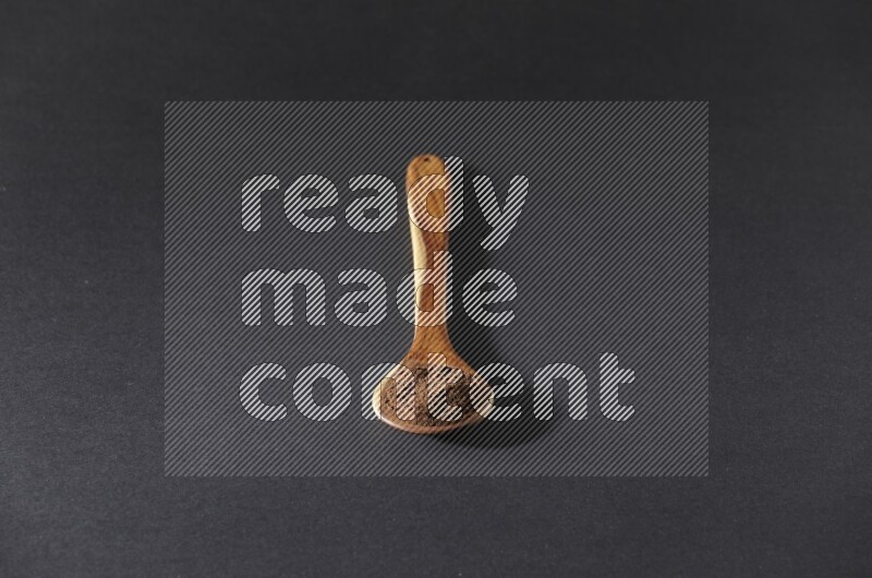 A wooden ladle full of cloves powder on a black flooring