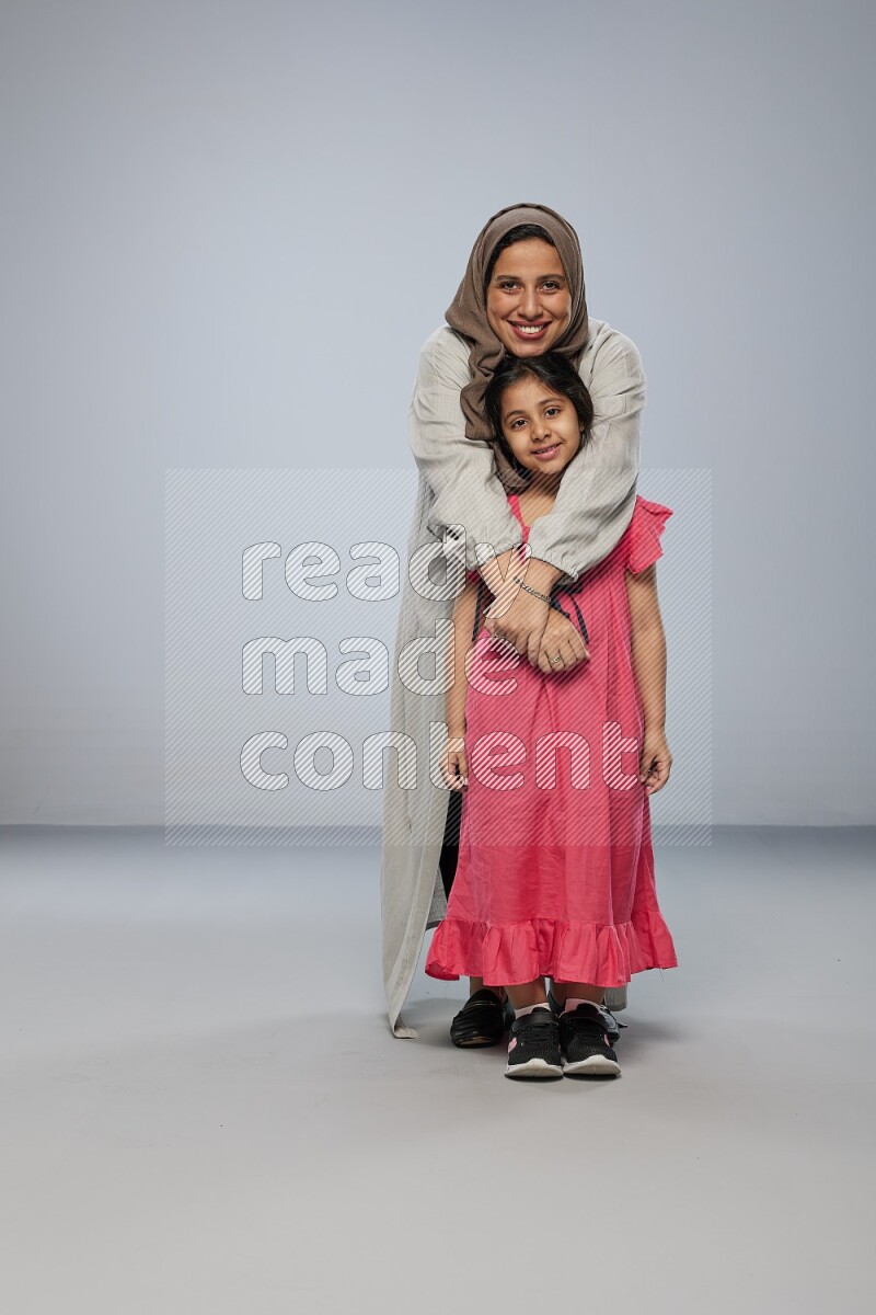 A girl and her mother interacting with the camera on gray background
