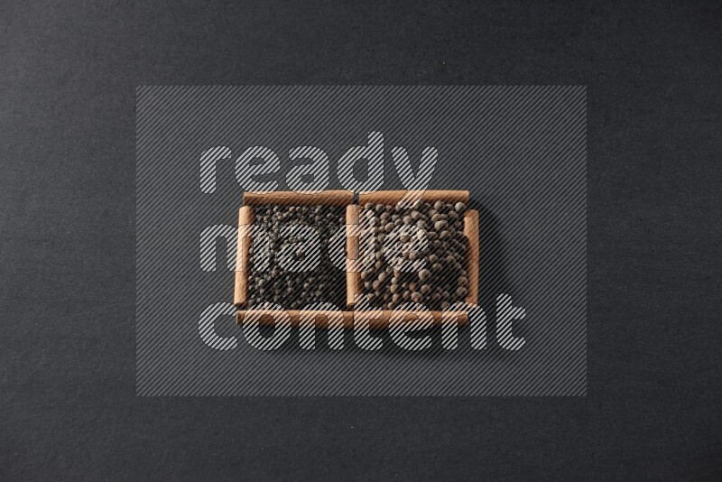 مربعان من أعواد القرفة ممتلئان بحبوب الفلفل الأسود وحبوب الفلفل الحلو علي خلفية سوداء