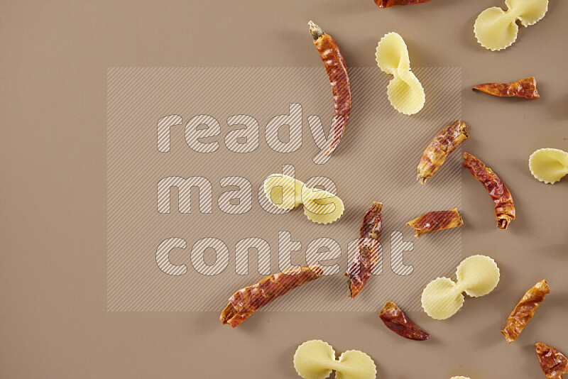 Raw pasta with different ingredients such as cherry tomatoes, garlic, onions, red chilis, black pepper, white pepper, bay laurel leaves, rosemary and cardamom on beige background