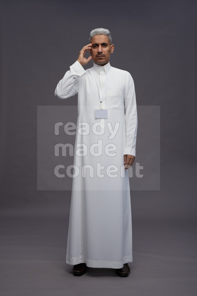 Saudi man wearing thob with neck strap employee badge standing interacting with the camera on gray background