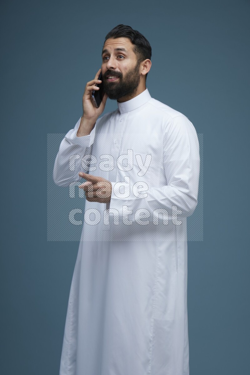 A man having a call on a blue background wearing Saudi Thob