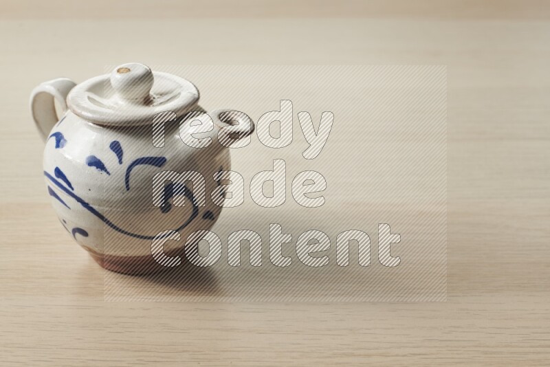 A pottery teapot on light wooden background