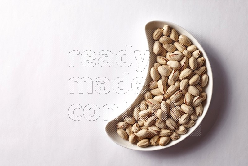 Pistachios in a crescent pottery plate on white background