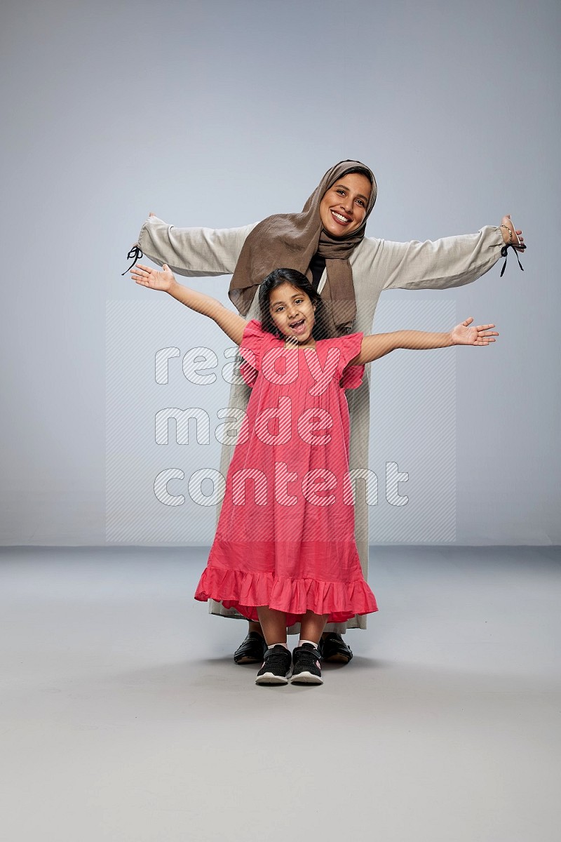 A girl and her mother interacting with the camera on gray background