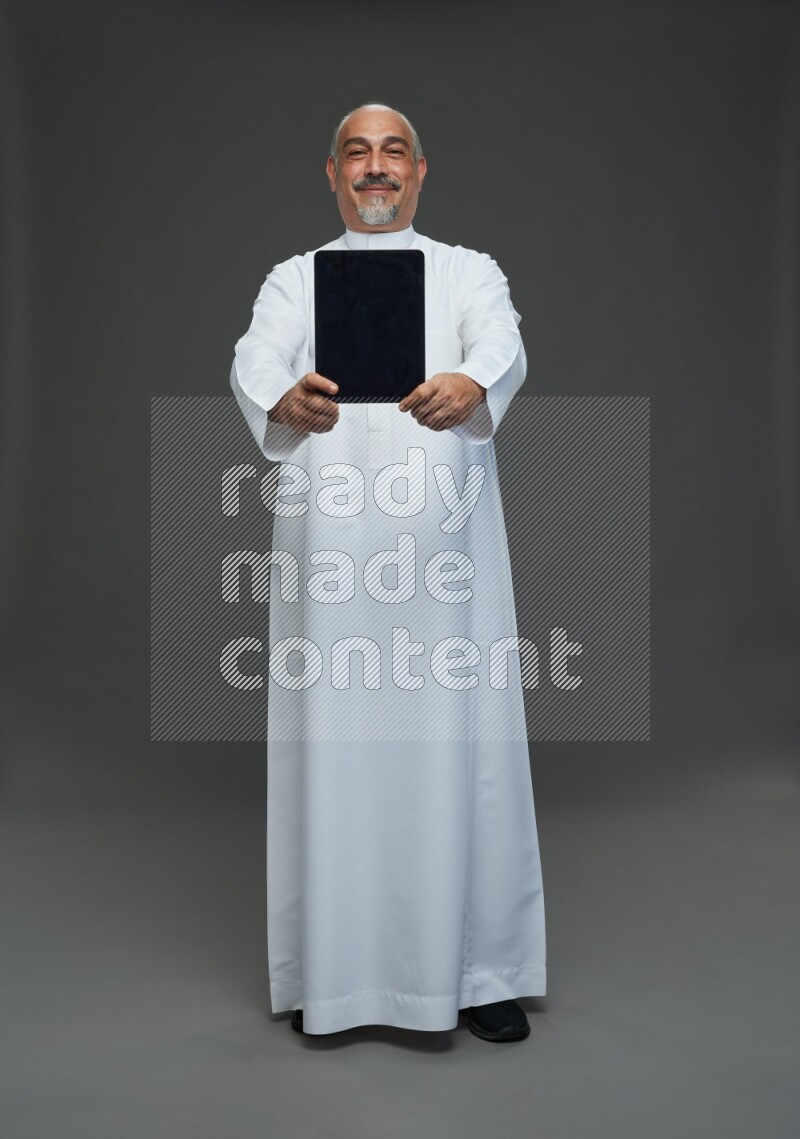 Saudi man without shomag Standing working on tablet on gray background