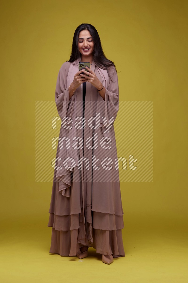 A woman Texting on a Yellow Background wearing Brown Abaya