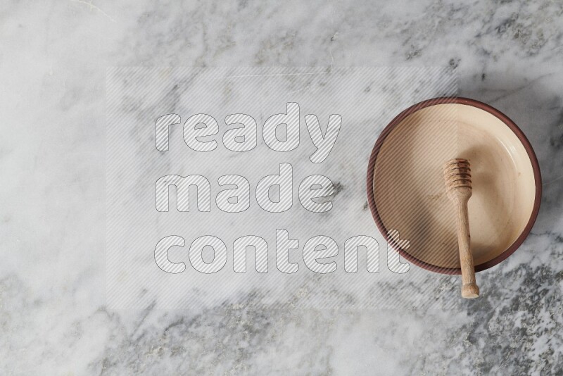 طبق فرن فخاري بيج مع ملعقة عسل خشبية بداخله على خلفية من الرخام الرمادي