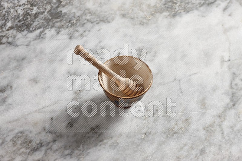 Decorative Pottery Bowl with wooden honey handle in it, on grey marble flooring, 65 degree angle