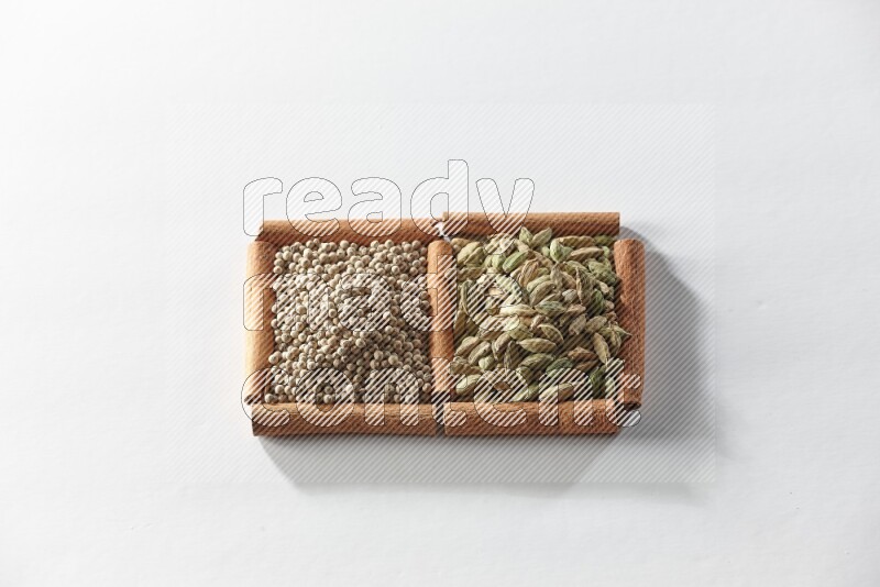 مربعان من أعواد القرفة ممتلئان بحبوب الهيل وحبوب الفلفل الأبيض علي خلفية بيضاء