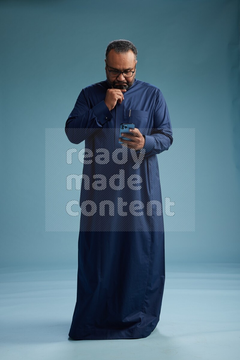 Saudi Man without shimag Standing texting on phone on blue background