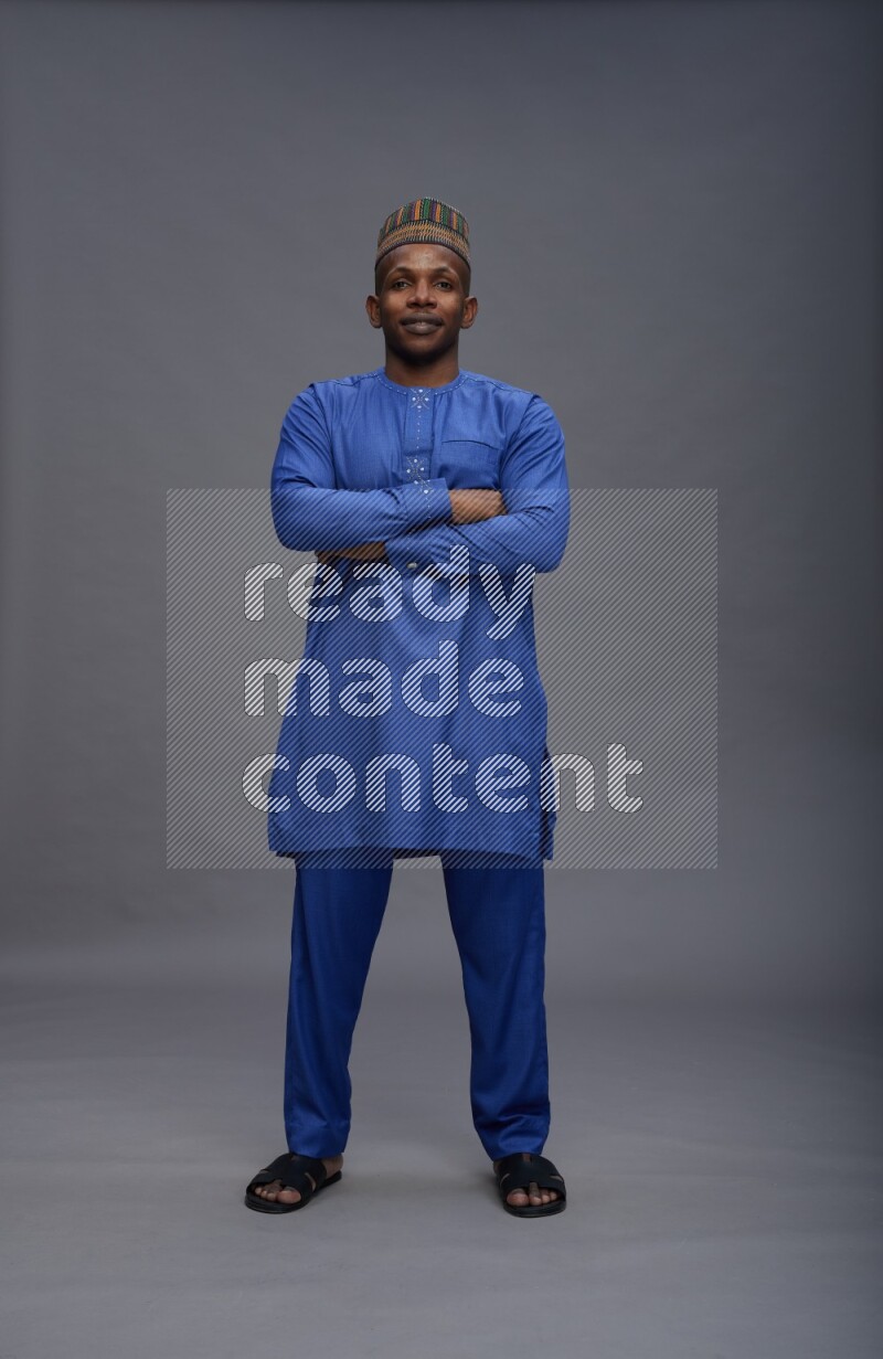Man wearing Nigerian outfit standing with crossed arms on gray background