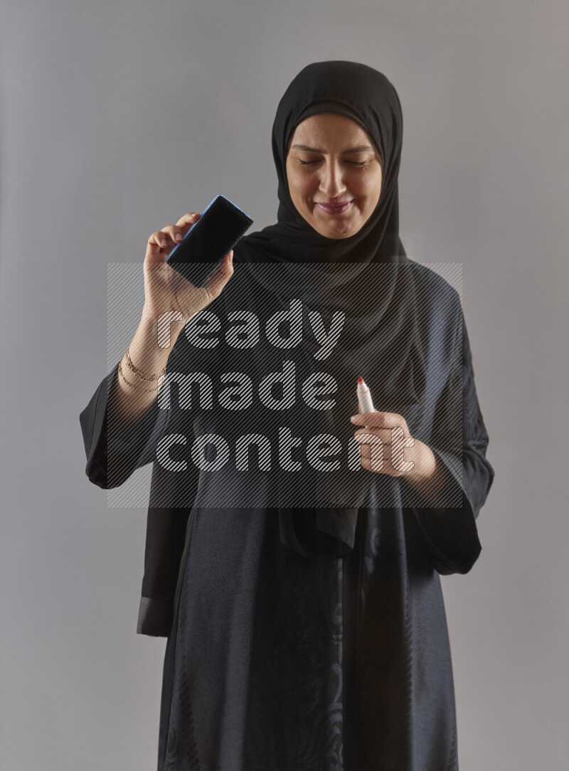 Woman in black abaya and hijab holding a marker pen to write on a transparent board with different reactions and expressions on grey background