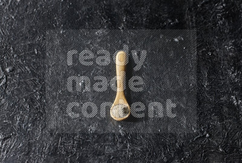 A wooden spoon full of white pepper powder on textured black flooring