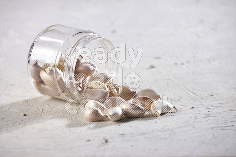 A glass jar full of garlic cloves flipped and the cloves came out on a textured white flooring