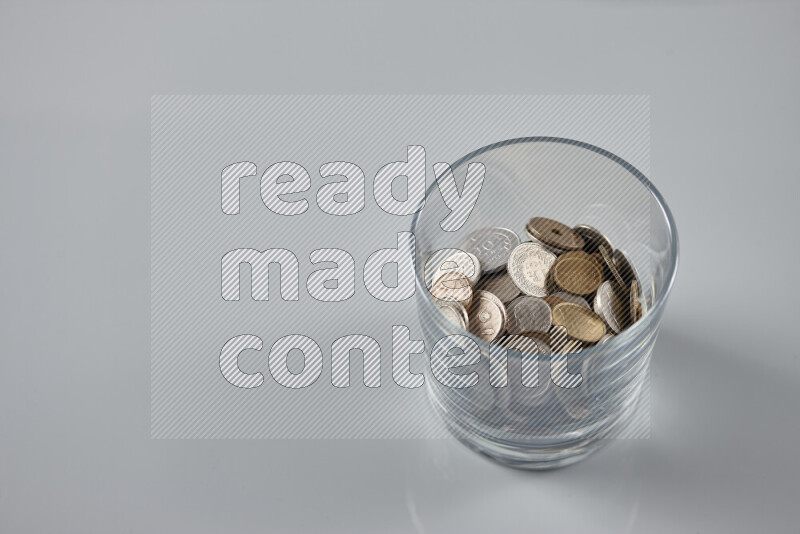 Random old coins in a glass cup on grey background
