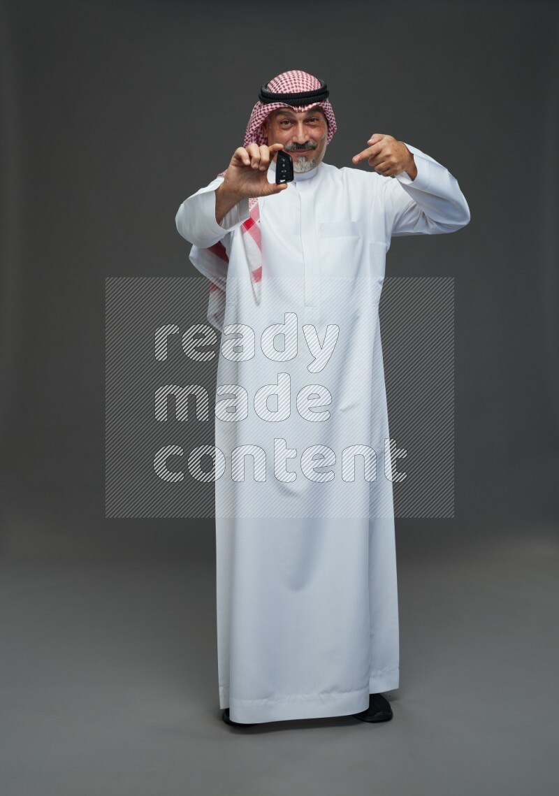 Saudi man with shomag Standing holding car key on gray background