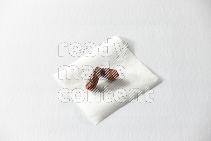 Two dried dates on a piece of paper on a white background in different angles