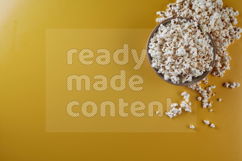 A brown pottery bowl full of popcorn with popcorn beside it on a yellow background in different angles