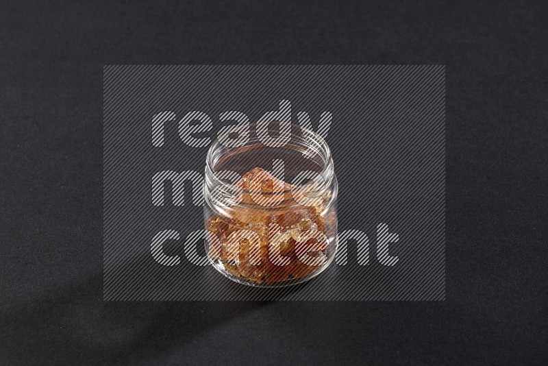 A glass jar full of gum arabic on black flooring