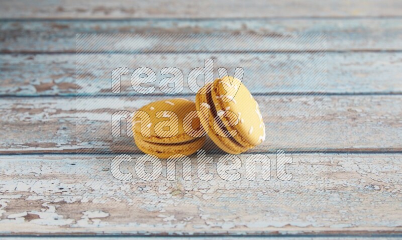 45º Shot of two Yellow Piña Colada macarons on light blue wooden background