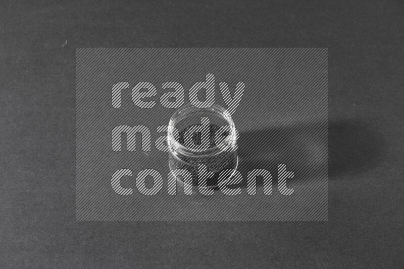 وعاء زجاجي ممتلئ ببذور حبة البركة علي خلفية سوداء