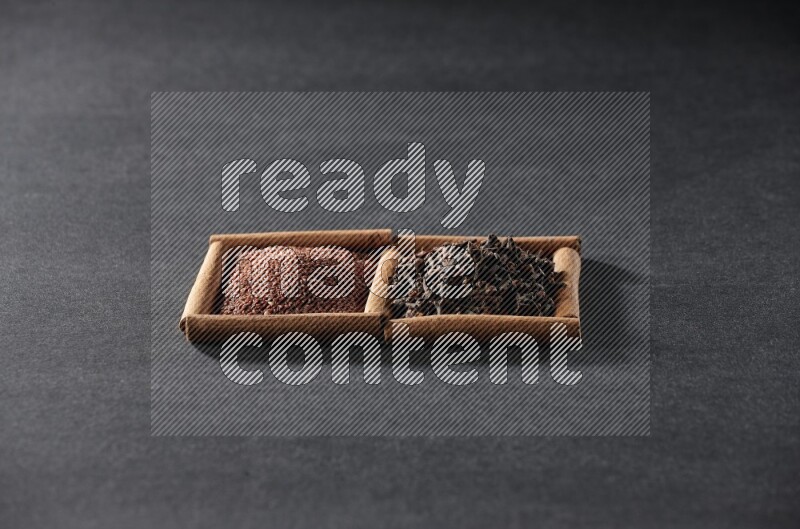 مربعان من أعواد القرفة ممتلئان بحب الرشاد والقرنفل علي خلفية سوداء