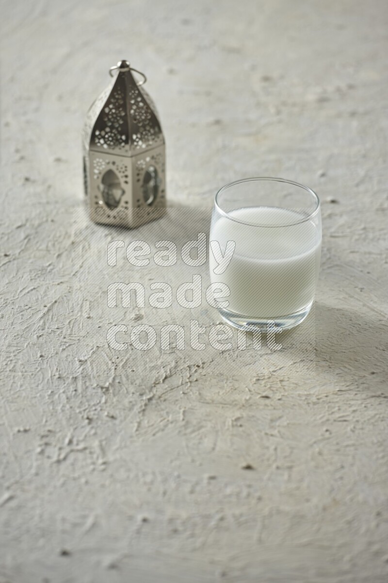 A silver lantern with different drinks, dates, nuts, prayer beads and quran on textured white background
