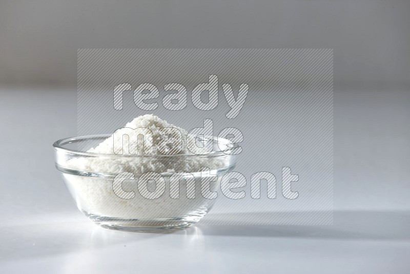 A glass bowl full of desiccated coconut on a white background in different angles