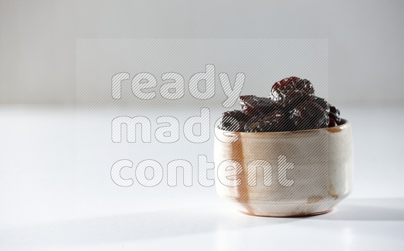 A beige ceramic bowl full of dried plums on a white background in different angles