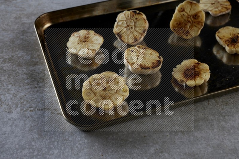 half's roasted garlic in a stainless tray on a grey textured countertop