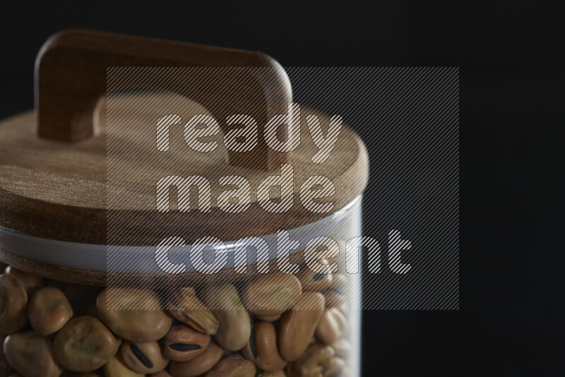 Fava beans in a glass jar on black background